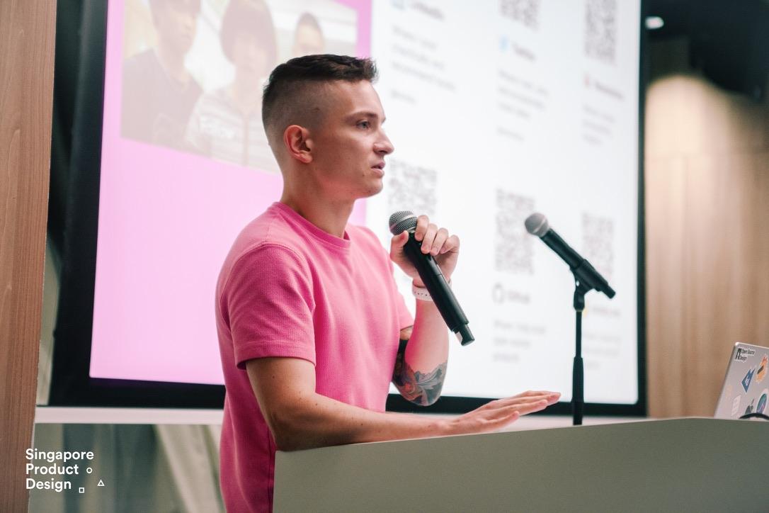 Young man in a bright pink shirt presenting and speaking into the microphone